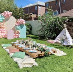 an outdoor party setup with balloons, pillows and table cloths on the grass in front of a teepee tent