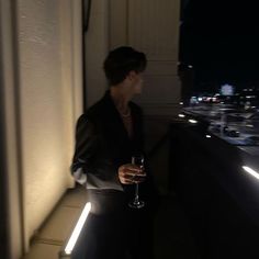 a woman holding a wine glass on top of a balcony at night with city lights in the background