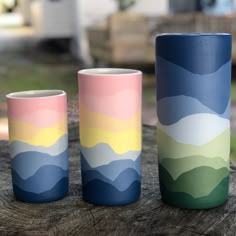 three colorful cups sitting on top of a tree stump