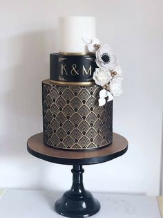 a black and gold wedding cake with white flowers on the top is sitting on a pedestal