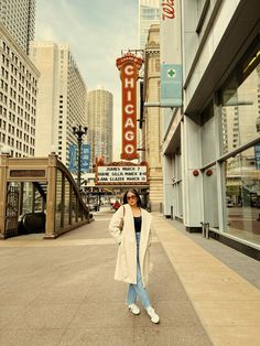 a woman standing on the sidewalk in front of a theater marquee and buildings