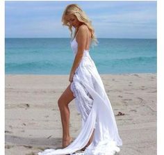 a woman standing on top of a sandy beach next to the ocean wearing a white dress