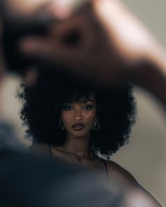 a woman with an afro is looking at her reflection in the mirror while she brushes her hair