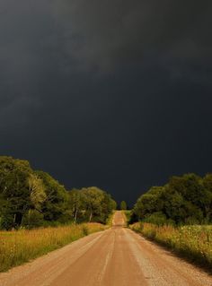 a dirt road surrounded by trees under a dark sky