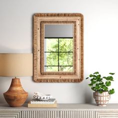 a mirror on the wall above a dresser with a lamp and potted plant next to it