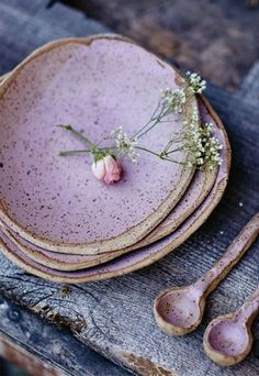 purple dishes with spoons and flowers sit on a wooden table top, ready to be used as place settings