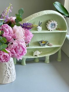 a vase filled with pink flowers sitting next to a green shelf and window sill