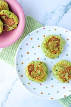 three crab cakes on a plate next to a pink bowl and green polka dot napkin