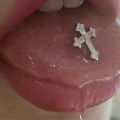 a close up of a person's tongue with a cross on it and water dripping from the lip