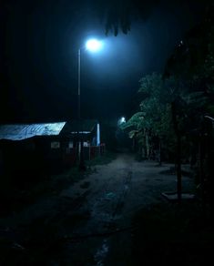 a dark street at night with a light on the pole and some houses in the background