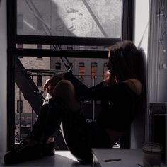 a woman sitting on a window sill looking out the window