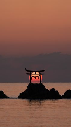 the sun is setting over an island with a tori - pole structure in the foreground