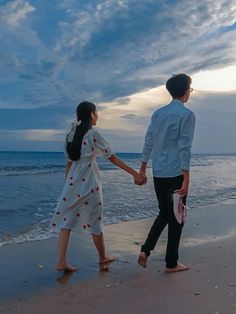 a man and woman holding hands walking on the beach at sunset with waves in the background