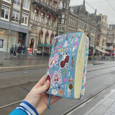 a person holding up a book with stickers on it in front of a city street