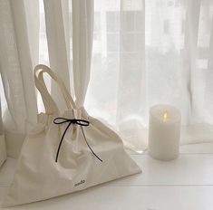 a white bag sitting on top of a table next to a candle and window sill