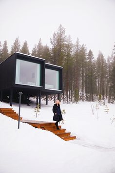 a woman sitting on steps in the snow near a house with a glass window and stairs leading up to it