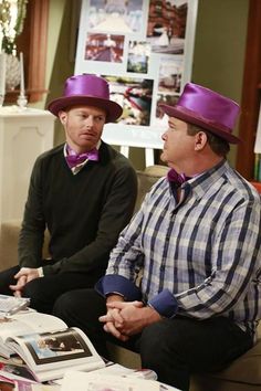 two men wearing purple hats sitting on a couch in front of a table with magazines