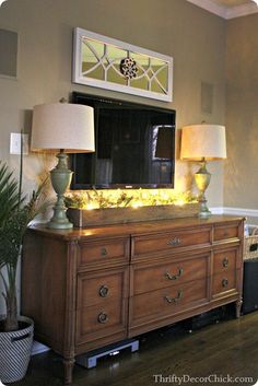 a dresser with two lamps on top of it and a mirror in the back ground