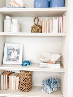 a white book shelf filled with books next to blue vases and other decorative items