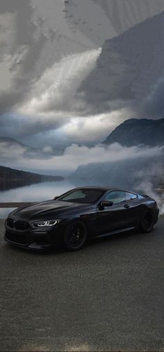 a black car driving down a road next to a mountain covered in fog and clouds