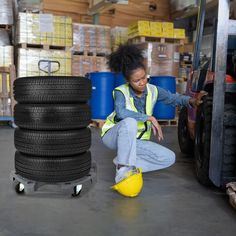 a woman in a yellow safety vest sitting on the ground next to a stack of tires