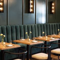 a restaurant with green velvet booths and wooden tables, white flowers in vases on the table