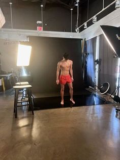 a man standing in front of a camera on a stage wearing red trunks and no shirt