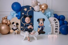 a baby is sitting on a chair in front of balloons and mickey mouses for his first birthday