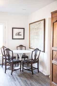 a dining room table with four chairs and a painting hanging on the wall above it