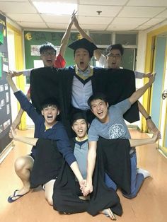 a group of people sitting on the floor with their arms in the air and wearing graduation caps