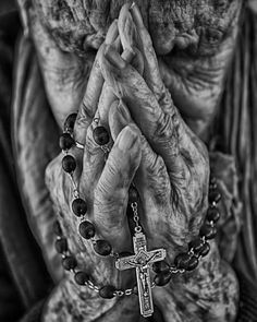 an old woman holding her hands to her face with a rosary around her neck and praying