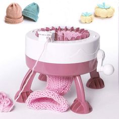 a pink and white crochet machine with several hats on the table next to it