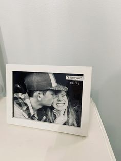 a couple kissing in front of a white photo frame on a table with a blue wall behind them