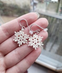 a hand holding two silver snowflake earrings