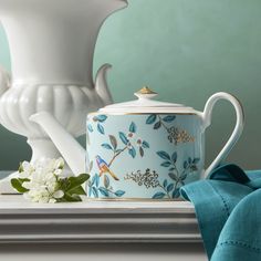 a tea pot with a bird on it next to a white vase and blue cloth