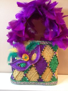 a purple and green purse with feathers on it's side sitting on a shelf