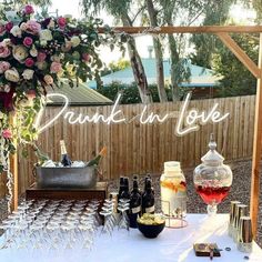 a table topped with lots of bottles of wine next to a wooden arbor covered in flowers