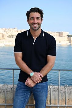 a man standing in front of the ocean with his hands on his hips and smiling