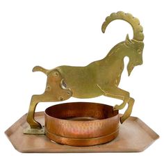 a brass statue of a ram standing on its hind legs with a bowl in front of it