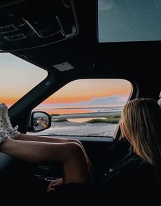 a woman sitting in the driver's seat of a car looking out at the ocean