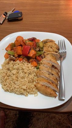 a white plate topped with chicken, rice and veggies next to a fork