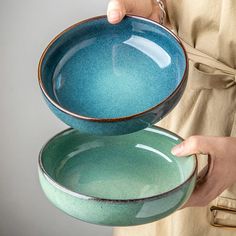 a person is holding two bowls in their hands, one blue and the other green