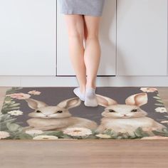 a woman standing on top of a rug with two bunnies in front of her