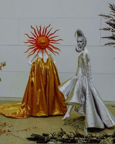 there are two mannequins dressed up in gold and silver dresses, one with a sun on it