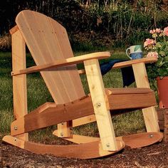 a wooden rocking chair sitting in the grass next to a potted plant and flowers