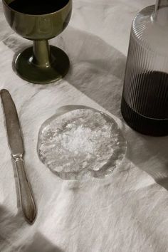 an empty plate and spoon on a white table cloth next to a wine glass, salt and pepper shaker