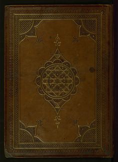 an old leather book with intricate designs on the front and back cover, sitting in a dark wood frame