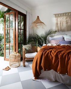 a bedroom with an orange blanket on the bed and some plants in the window sill