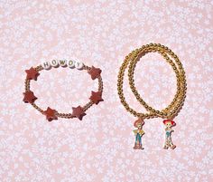 two bracelets with charms on them sitting next to each other in front of a pink background