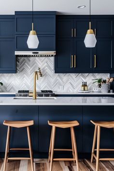 a kitchen with blue cabinets and wooden stools next to the counter top, along with two pendant lights hanging from the ceiling